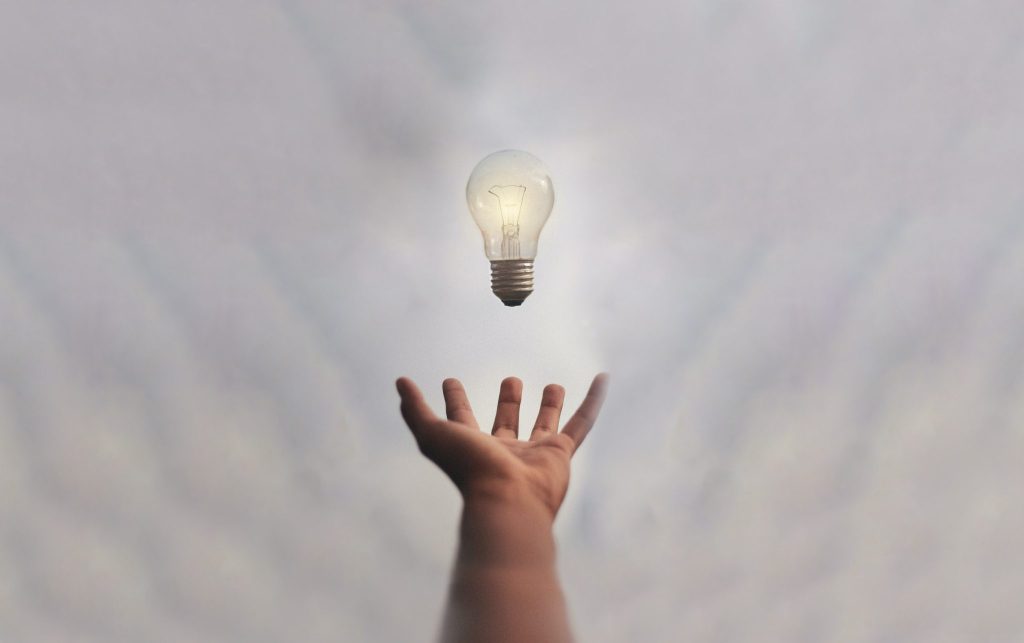 Eine Hand wirft eine leuchtende Glühbirne in die Luft